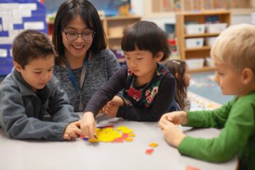 istockphoto-2170612428-612×612 Asian young woman teacher with Asian Caucasian multiracial preschool kindergarten students learning playing with puzzle toy in classroom